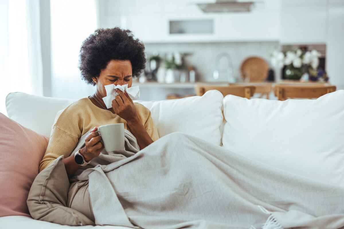 Woman sitting on a couch blows her nose
